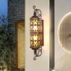 Đèn gắn tường SL-Temple2590 khung nâu sáng vàng ấm trên tường trắng cạnh ô cửa tròn lúc chạng vạng